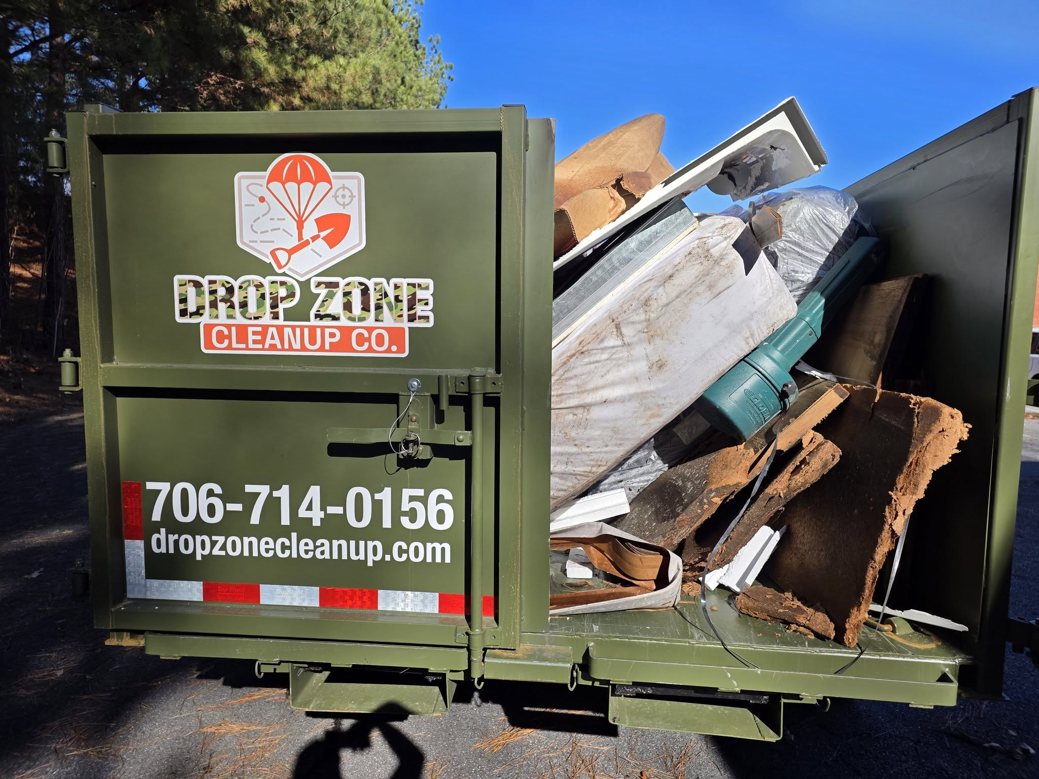 Drop Zone Cleanup Co. branded dumpster loaded with construction debris